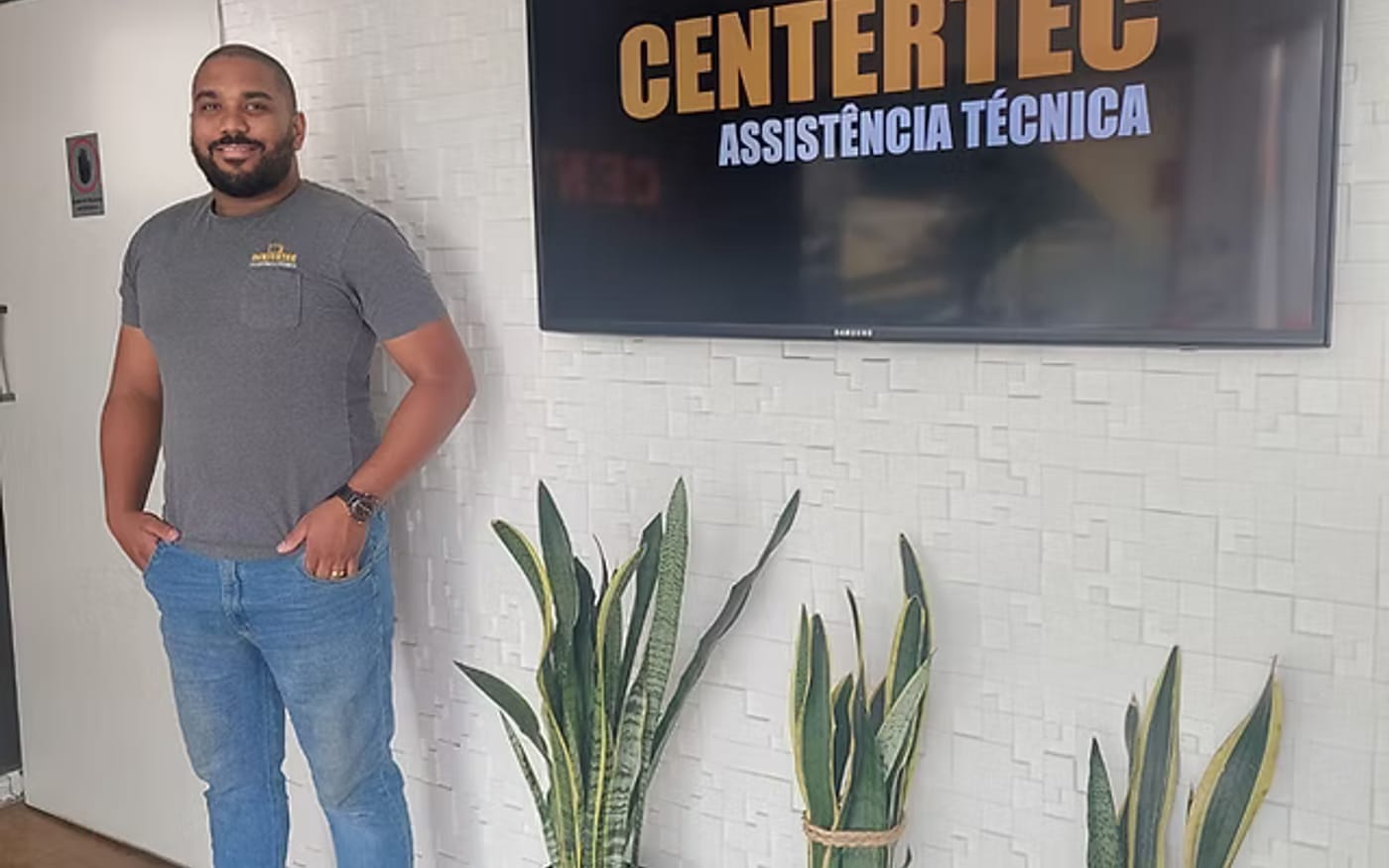 Atendente da Centertec na loja, ao lado da marca na parede
